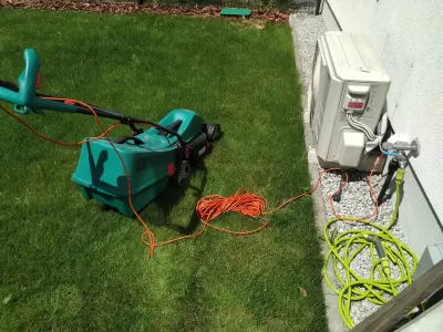 5 Melhores Cortadores De Grama Para O Seu Pequeno Jardim : Um cortador de grama elétrico Bosch conectado ao ar livre em um pequeno gramado do jardim
